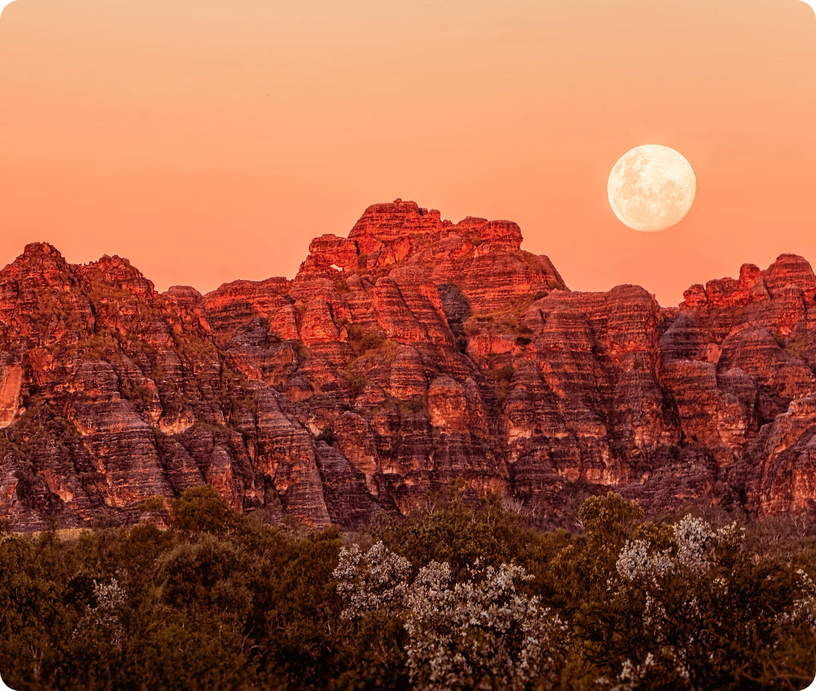 Full moon over rugged mountains with a sunset sky.